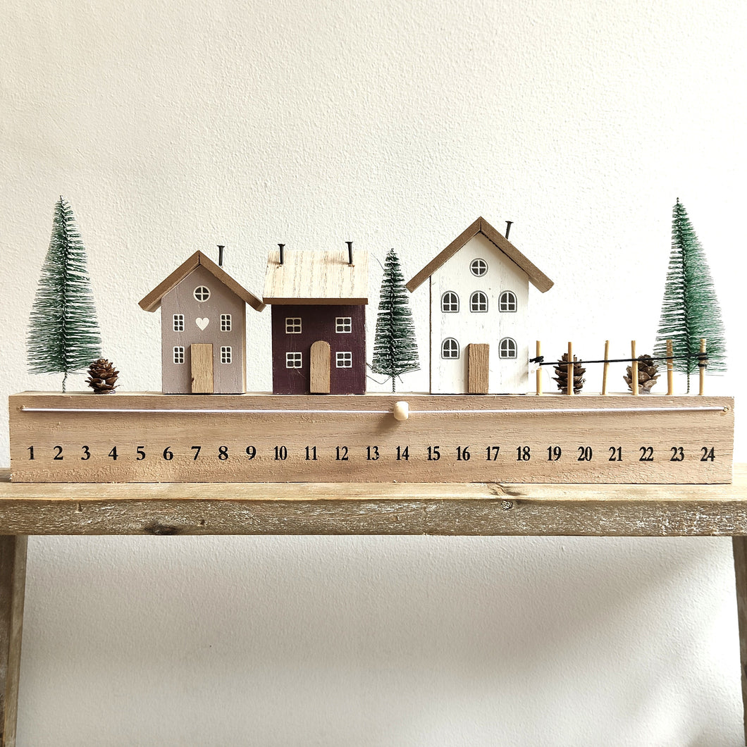 Decorative wooden advent calendar with houses and trees on a white background by Heaven Sends